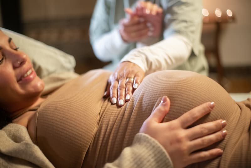 Cropped Image Smiling Pregnant Woman Midwife Home Woman Casual Clothes Lying Bed Midwife Holding Hand Pregnancy Medicine Home Birth Concept (1)